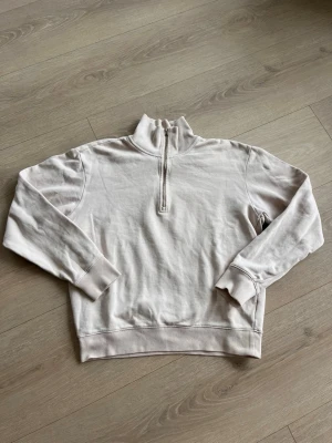 Beige halfzip från Tiger of Sweden - Säljer en beige halfzip hoodie från Tiger of Sweden. Tröjan har hög krage med dragkedja, långa ärmar och diskret logga på bröstet. Tillverkad i mjukt bomullsmaterial och har ribbade muddar vid ärmslut och nederkant. Perfekt för en clean och stilren look.