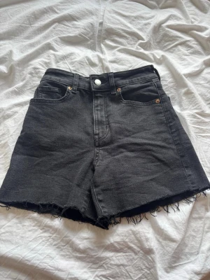 Svarta högmidjade jeansshorts - Säljer ett par svarta högmidjade jeansshorts med råa, fransiga kanter. Klassisk femficksmodell med knapp och dragkedja framtill. Perfekta för sommaren och ger en avslappnad vibe till din outfit. Väldigt bekväma och använd endast två gånger. Köpt på HM omedveten om nypris men säljer för 39 kr. 
