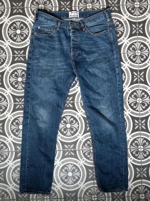 Blå raka jeans från Acne Studios - Säljer ett par klassiska blå jeans från Acne Studios med rak passform och fem fickor. Jeansen har en snygg tvättad look och är tillverkade i denim. Perfekta för dig som gillar stilrena och tidlösa plagg.