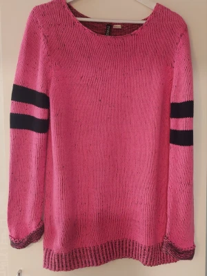 Rosa stickad tröja. - Stickad tröja i en jätte fin rosa färg med rund halsringning och långa ärmar. Tröjan har svarta ränder på ärmarna och ribbstickade muddar i ärmslut och nederkant.  Knappt använd så är i jötte fint skick. ( det är skuggor från kameran som gör att det ser ut som det är lite mörkare längst ner, finns inga fläckar, se sista billden där syns det bättre hur den ser ut och är inga skuggor från kameran)  Från rök och djurfritt hem.
