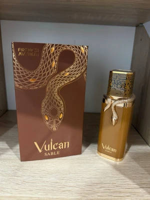 Vulcan Sable parfym med orm-detalj - Lyxig parfymflaska i guld och brunt från Vulcan Sable. Flaskan har en unik orm-detalj i guld runt halsen och ett elegant mönstrat lock. Kommer i en snygg brun förpackning med guldfärgad orm och text. Perfekt för dig som gillar exklusiva dofter och cool design.