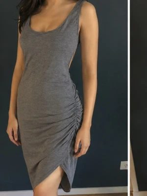 Ljus Grå klänning  med öppen rygg strl M - Snygg ljus grå klänning i mjukt material och rynkning på sidan. Klänningen är ärmlös och har en djup öppen rygg, vilket ger en modern och trendig look. Perfekt för dig som gillar stilrena och bekväma plagg. Ny men saknar pristagg 