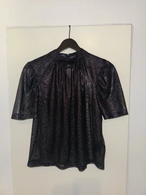 Glittrig svart mesh topp - Säljer en glittrig svart mesh topp med korta ärmar. Toppen har en lätt transparent look.
