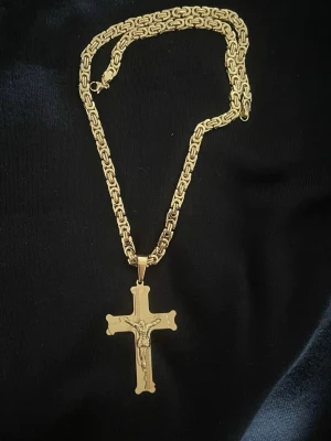 Byzantinsk Halskedja 18k Guldpläterad - Snyggt halsband i guldfärg med ett detaljerat korshänge som har Jesusmotiv. Kedjan har ett unikt, robust mönster som ger ett exklusivt intryck. Perfekt för dig som vill ha ett statement-smycke med religiös touch. Materialet ser ut som metall med blank finish.