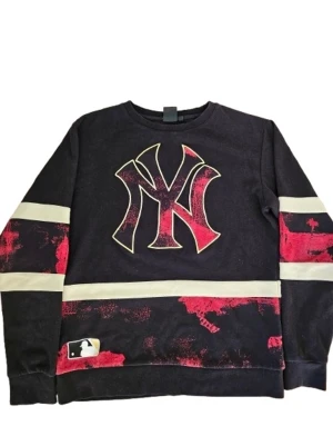 New York Yankees tröja - Cool svart långärmad topp med stort New York Yankees-tryck framtill och texten 'NEW YORK' på ryggen. Har röda och vita detaljer samt breda ränder på ärmar och nederkant. Perfekt för dig som gillar sportig streetstyle.