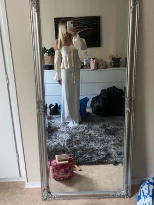 Offshoulder cremevit topp - Säljer en söt offshoulder kortklänning i vit färg med långa, vida ärmar och snörning framtill. Klänningen har en figurnära passform och volangdetaljer upptill. Perfekt för sommarens alla tillfällen!
