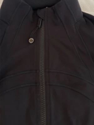 Svart vindjacka från Lululemon - Snygg svart vindjacka från Lululemon med hög krage och hel dragkedja framtill. Jackan har figurnära passform, långa ärmar och två fickor med dragkedja. Perfekt för dig som gillar sportig och stilren look.
