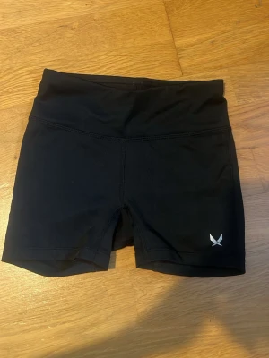 Svarta träningsshorts från SOC - Snygga svarta träningsshorts från SOC med hög midja och diskret logga på benet. Tillverkade i stretchigt funktionsmaterial som passar perfekt för gym, löpning eller annan träning. Klassisk och enkel design som är lätt att matcha.