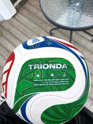 Vit och grön fotboll Trionda - Säljer en fotboll i modellen Trionda Competition. Bollen är vit med gröna, röda och blå detaljer samt text och mönster. Perfekt för matcher eller träning på planen. Officiell matchboll-replika med FIFA-logga. Helt ny utan prislapp priset kan diskuteras . Säljer den då jag inte gillar fotboll 