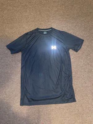 Svart tränings-tshirt  - Säljer en svart tränings-tshirt  i funktionsmaterial. T-shirten har rund halsringning, korta ärmar och en diskret logga på bröstet. Perfekt för gymmet eller löprundan.
