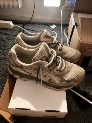  ASICS nyc oyster grey  dubbel laces  - Snygga beige ASICS sneakers med meshpaneler och syntetiska detaljer. Skorna har en chunky sula och klassisk snörning. Perfekta för dig som gillar sportig stil och vill ha bekväma skor till vardags. Ikonisk ASICS-logga på sidan.