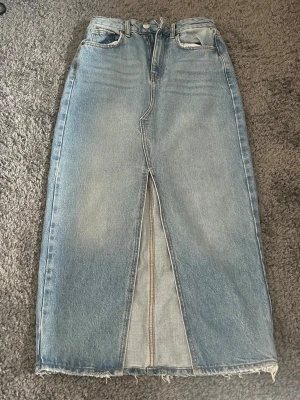 Ljusblå jeanskjol med slits - Säljer en ljusblå jeanskjol i rak modell med rå kant nertill och en snygg slits framtill, har några fläckar som inte är jätte tydliga (kolla bild 3) men som jag skulle tro går bort efter att ha tvättat några gånger💕💕