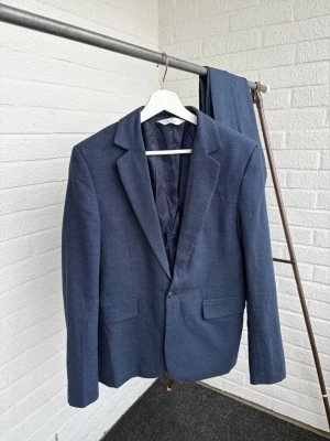 Mörkblå Linnekostym från H&M - Snygg mörkblå kostym från H&M med klassisk kavaj och matchande byxor. Kavajen har två fickor framtill, enkelknäppning och är helfodrad. Perfekt för dig som vill ha en stilren och tidlös look.