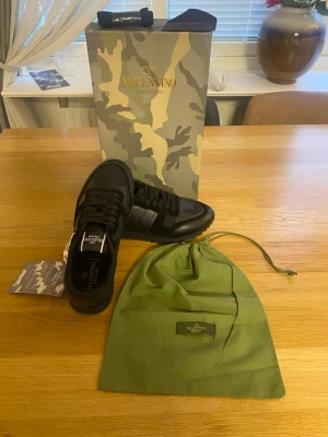 Valentino Rockrunners - Snygga svarta sneakers från Valentino Garavani med kamouflagemönster och detaljer i mocka och läder. Skorna har svarta skosnören, robust sula och klassisk låg profil. Perfekta för dig som vill ha en exklusiv och trendig look.