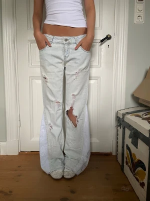 Ljusblå lågmidjade jeans med spets - Säljer dessa såå snygga och unika jeans som är omsydda till bootcut med spets tyg. Jeansen är ljusblå och har slitningar på benen. Midjemått 39 cm och innerbenslängd 83 cm. Obs jeansen har en liten fläck vid framfickan, se sista bilden. Kontakta mig gärna privat vid frågor eller liknande💓