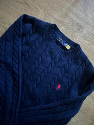 Mörkblå kabelstickad tröja Polo - Mörkblå kabelstickad tröja från Polo Ralph. Perfekt inför hösten/vintern då den både är skön och varm. Vid minsta fundering hör av dig!                          (Endast använd några få gånger)