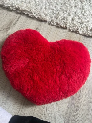 Röd hjärtformad vete kudde - Mysig hjärtformad kudde i mjukt, fluffigt rött tyg. Perfekt som dekoration i soffan eller på sängen. Kudden har en tydlig hjärtform och är tillverkad i ett plyschliknande material som känns skönt att ta på.