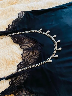 Silverfärgat halsband med droppformade detaljer - Säljer ett chunky halsband i silverfärg med kedjedesign och droppformade detaljer längs hela halsbandet. Halsbandet har en modern och edgy look som passar perfekt till olika stilar. Materialet är metall och designen är unik och trendig.