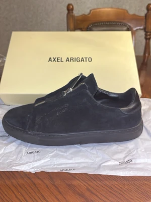 Svarta sneakers från Axel Arigato - ! DOM ÄR LITE SÖNDER KOM PV FÖR SVAR !  Stilrena svarta sneakers från Axel Arigato i mocka och läder. Skorna har en låg siluett och coola dragkedjor istället för klassiska snören. Perfekta för dig som gillar minimalistisk och modern design.