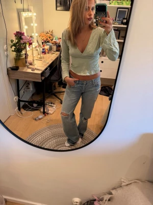 Ljusgrön omlottopp med v-ringning - Säljer en ljusgrön omlottopp med v-ringning och långa ärmar. Toppen har knyt i ryggen och är croppad, vilket ger en trendig och avslappnad look. Perfekt för dig som gillar stilrena och bekväma plagg i garderoben.