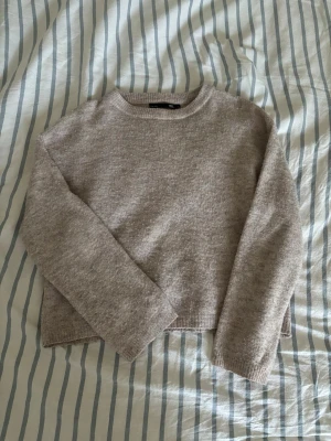 Babyrosa stickad  - Mysig beige stickad tröja från 157 med rund halsringning och långa ärmar. Tröjan har en enkel, rak passform och ribbade muddar vid halsen. Perfekt för lager på lager och en avslappnad stil.