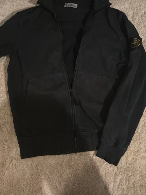 Stone island tröja - Äkta stone island fullzip i färgen svart och storlek M, skick 7/10. Tröjan väldigt skön och håller än varm, därav väldigt bra nu till hösten/vintern. Pris kan diskuteras.