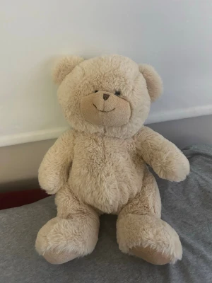 Mjuk nalle från Teddykompaniet - Söt och fluffig beige nallebjörn från Teddykompaniet. Nallen har rund form, mjuk päls och ett broderat leende ansikte. Perfekt som gosedjur eller dekoration i sovrummet. Märkt med Teddykompaniets etikett på sidan.