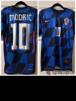 Kroatien fotbollströja Modrić #10 - Säljer en blå och svart rutmönstrad fotbollströja från Nike med Kroatiens landslagsemblem och Modrić #10 tryckt på ryggen. Tröjan har röda detaljer och är tillverkad i ett lätt, snabbtorkande material med Dri-FIT-teknologi.