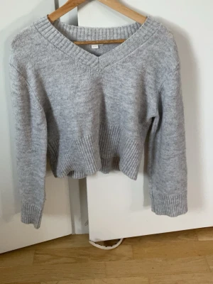 Ljusgrå stickad tröja Gina Tricot - Mysig ljusgrå stickad tröja från Gina Tricot med v-ringning och bred ribbstickad kant vid ärmslut och nederkant. Tröjan har en avslappnad passform och är perfekt för kyliga dagar. Materialet känns mjukt och behagligt mot huden.