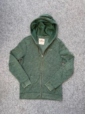 Grön zip hoodie från Hollister - Säljer denna Snygga gröna hoodie från Hollister i jätte bra skick och till bra pris,         Skick 9/10. Storlek S men sitter lika bra som en M Bara att skriva vid några funderingar!