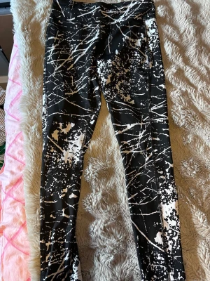 Svarta leggings med vit splatter - Snygga svarta leggings från FIRMILIFE med vitt splattermönster och hög midja. Tillverkade i stretchigt material som sitter skönt och följer kroppen. Perfekta för dig som gillar en sportig och trendig look.