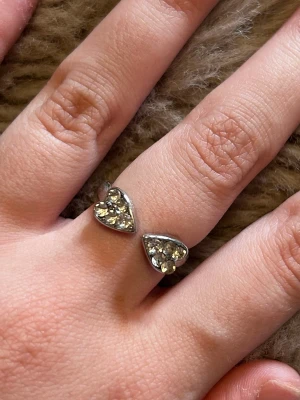 Silverring med hjärtformade stenar - Snygg silverfärgad ring med två hjärtformade detaljer fyllda med gnistrande klara stenar. Ringen är öppen framtill och har en modern, trendig design som sticker ut. Perfekt för dig som gillar unika accessoarer och vill addera lite extra bling till din stil.