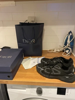 Svarta  sneakers med vita detaljer - Säljer ett par svarta m sneakers med vita kontrastdetaljer och tjock sula. Skorna har en sportig design med rund tå och snörning. Materialet är en mix av textil och läder. -logga syns på sidan och sulan. Perfekta för dig som gillar exklusiva streetwear-vibbar. Passar dig som bör 45 men står strl 46