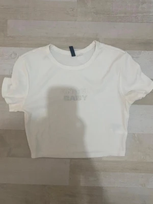 Vit croppad topp med text - En vit croppad topp med korta ärmar och broderad text 'ANGEL BABY' framtill. Från hm 