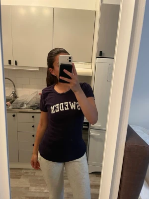 Mörkblå t-shirt med SWEDEN-tryck - Snygg mörkblå t-shirt med vit SWEDEN-text på bröstet. Klassisk rund halsringning och korta ärmar. Perfekt för dig som vill visa lite svensk stolthet på ett stilrent sätt.