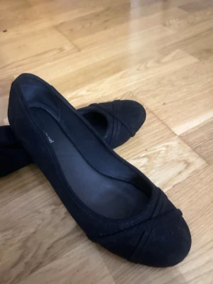 Svarta ballerinaskor från Graceland - Säljer ett par klassiska svarta ballerinaskor från Graceland. Skorna har rund tå och dekorativa sömmar framtill. Tillverkade i textilmaterial med enkel och stilren design som passar till det mesta. 