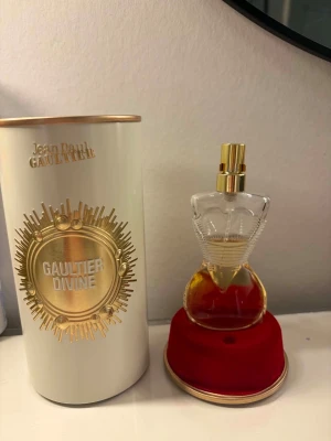 Jean Paul Gaultier Gaultier Divine EdP - Exklusiv parfym från Jean Paul Gaultier, Gaultier Divine EdP, 30 ml. Flaskan har en unik design i form av en kvinnokropp med gulddetaljer och står på en röd sammetsliknande bas. Förpackningen är vit och guld med elegant präglad text.Doft:tänk söt vanilj + vita blommor + varm, krämig huddoft, med en liten salt friskhet.Ungefär hälften kvar