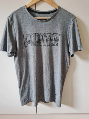 Grå t-shirt från Puma strl S - Säljer en grå t-shirt från Puma med stort tryck på bröstet. T-shirten har rund halsringning och korta ärmar. Material 100% bomull. Storlek S.
