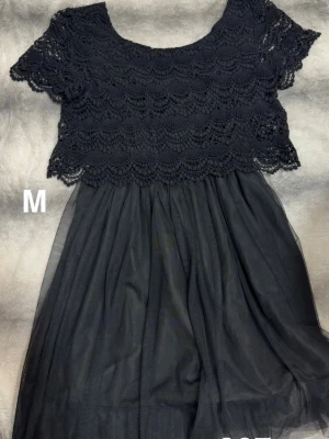 Svart spetsklänning med kort ärm - Snygg svart klänning med överdel i virkad spets och korta ärmar. Kjolen är i tunt, flowy tyg som ger en luftig känsla. Perfekt för dig som gillar en feminin och elegant stil.🌸 Sparsamt använd. Storlek m