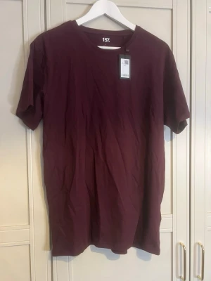 Vinröd t-shirt från 157 - Enkel och stilren vinröd t-shirt från 157 med rund hals och korta ärmar. Tillverkad i mjuk bomull som känns skön mot huden. Perfekt basplagg att ha i garderoben.