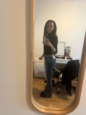 Blå bootcut jeans med låg midja - Säljer ett par blå bootcut jeans med låg midja och klassiska fickor både fram och bak. Jeansen har en snygg tvätt och sitter tajt över höfterna innan de blir vidare nedtill. Perfekta för dig som gillar retrostil och vill ha ett par jeans som sticker ut. I princip helt nya, endast använt 3 gånger och har inga skador eller flisor. 