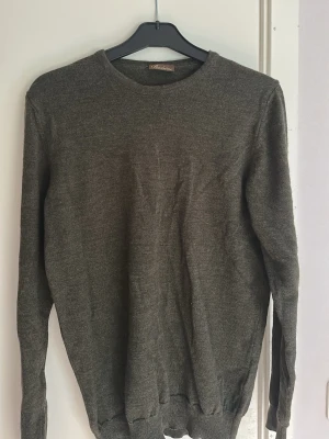 Olivgrön stickad tröja Stenströms - Snygg olivgrön stickad tröja från Stenströms med rund halsringning. Tröjan har långa ärmar och ribbade muddar vid ärmslut och nederkant. Perfekt för lager på lager och enkel att matcha med olika outfits. Fint skick!