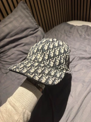  keps från Dior - Säljer en snygg keps från Dior med klassiskt blått och vitt monogrammönster. Kepsen har böjd skärm och justerbar passform. Tillverkad i ett slitstarkt tyg med exklusiv känsla och fodrad insida med diskret Dior-logga.