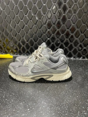 Grå Nike sneakers med mesh och reflex - Säljer ett par grå Nike sneakers med meshpaneler och reflexdetaljer. Skorna har en chunky sula i beige och silverfärgade inslag på hälen. Klassisk Nike Swoosh på sidan och bekväm vadderad plös. Perfekta för dig som gillar sportig och trendig stil.
