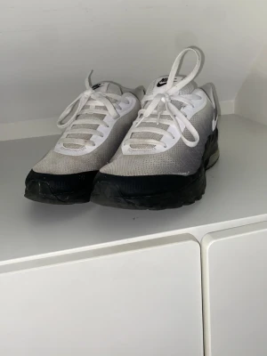 Nike vita och grå sneakers - Snygga sneakers från Nike i vitt och grått med svart sula. Ovandelen är i meshmaterial för bra ventilation och har klassisk snörning. Perfekta för dig som gillar stilrena och sportiga skor med en chunky sula. Dom har dock små hål på sidan som man ser på bilderna syns inte när man har på sig dom.