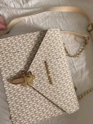   axelväska - Snygg beige axelväska med guldiga detaljer och kedja. Väskan har ett diskret -mönster, guldfärgat spänne och justerbar axelrem i både läder och kedja. Insidan har ett litet fack för småsaker. Perfekt för dig som gillar stilrena accessoarer.
