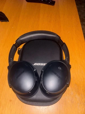 Bose svarta over-ear hörlurar - Snygga svarta over-ear hörlurar från Bose med mjuka, vadderade kåpor och justerbar bygel. Kommer med ett matchande hårt fodral med Bose-logga. Perfekta för att lyssna på musik eller poddar med grym komfort och stilren design.