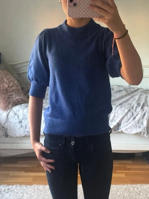 Blå stickad tröja med puffärm - Snygg blå stickad tröja med puffärmar och ribbade muddar vid ärmslut och midja. Tröjan har en högre rund halsringning och är gjord i ett mjukt material som känns skönt mot huden. Perfekt för dig som vill ha en enkel men trendig look!💕