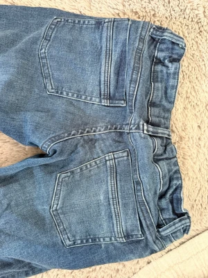 Blå klassiska jeans bootcut - Säljer ett par blå jeans med raka ben och fem fickor. Jeansen har låg midja, bälteshällor och dragkedjegylf. Materialet är klassisk denim i bomull med snygga slitningar och tvättade detaljer. Perfekta för en avslappnad och trendig look. Ltb liknande från Gina i storlek 158