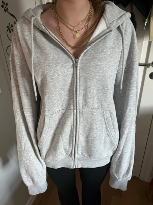Ljusgrå zip hoodie med huva - Ljusgrå hoodie med dragkedja framtill och två fickor. Tröjan har en stor huva med dragsko och ribbade muddar vid ärmslut och nederkant. Tillverkad i mjukt sweatshirtmaterial, perfekt för en avslappnad stil. Oversized 
